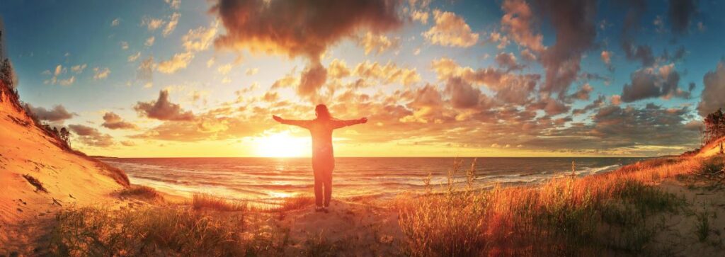 Symbolic image of a person standing in front of a vibrant sunset with arms outstretched, representing freedom and hope in the context of foreclosure prevention.